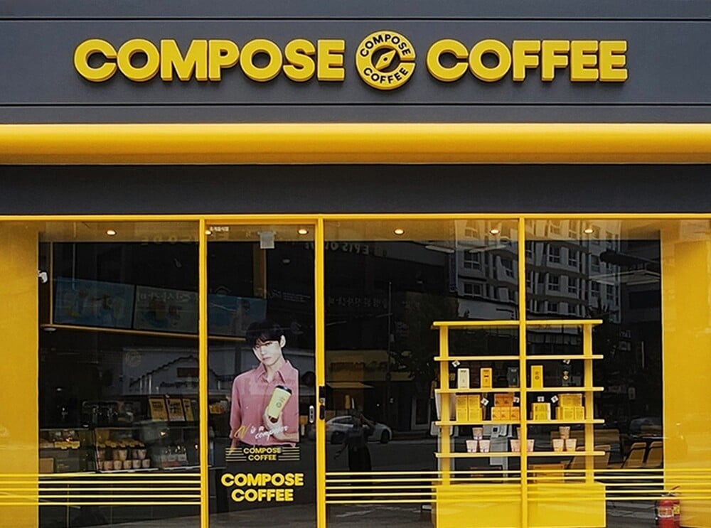 Façade jaune et noire d'un café Compose Coffee en Corée du Sud, avec une vitrine affichant Kim Taehyung (김태형), V de BTS et des produits de la marque.