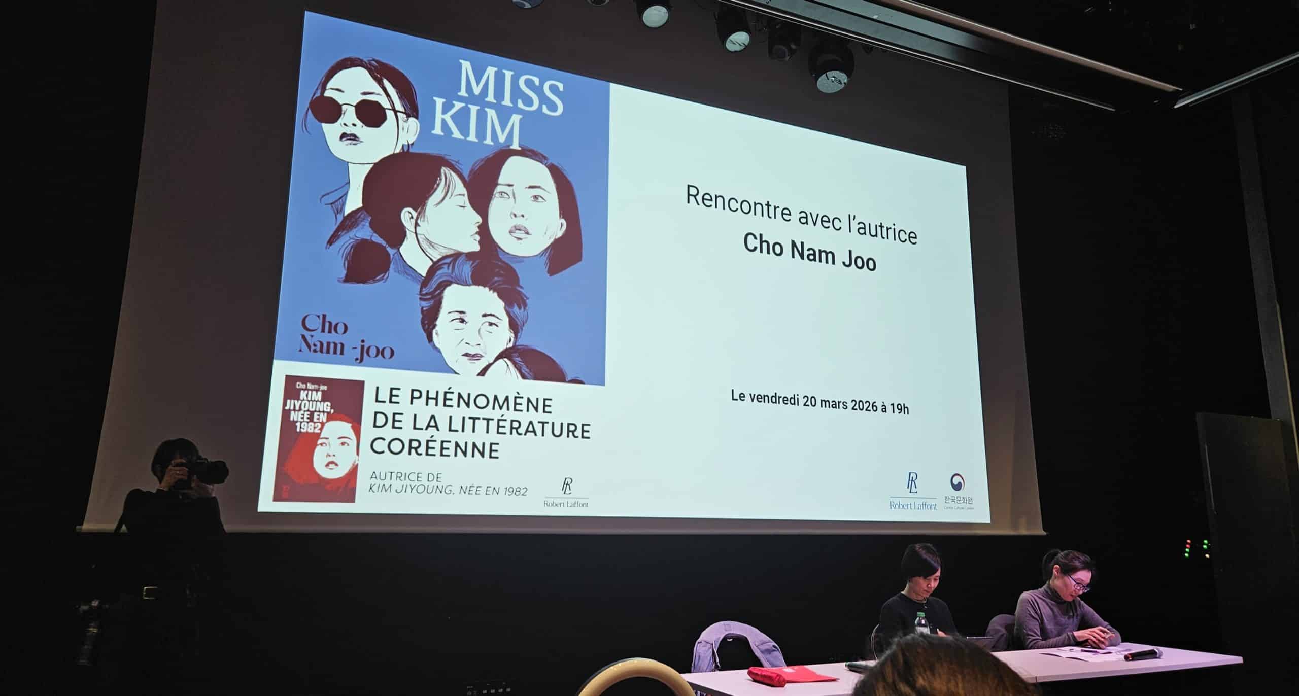 Vue d'ensemble d'une salle de conférence dans l'auditorium du Centre Culturel Corée avec une diapositive de présentation concernant la rencontre avec l'autrice Cho Nam-Joo. Couverture du recueil de nouvelles Miss Kim. Au premier plan, l'autrice Cho Nam-Joo et assise à côté de son interprète.