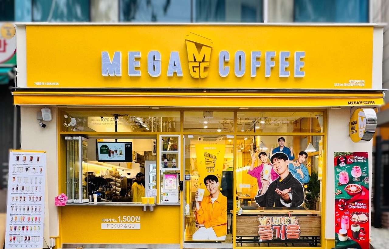 Façade jaune vif d'un café Mega Coffee en Corée du Sud, avec des affiches de célébrités en vitrine.