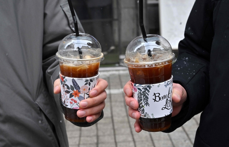 Deux personnes tenant chacune un americano glacé dans un gobelet en plastique avec une manchette fleurie, dans une rue de Corée du Sud