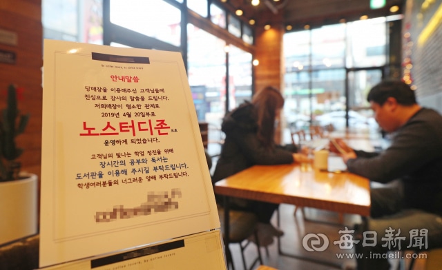 Panneau "노스터디존" (No Study Zone) posé sur une table dans un café coréen, avec des clients en arrière-plan